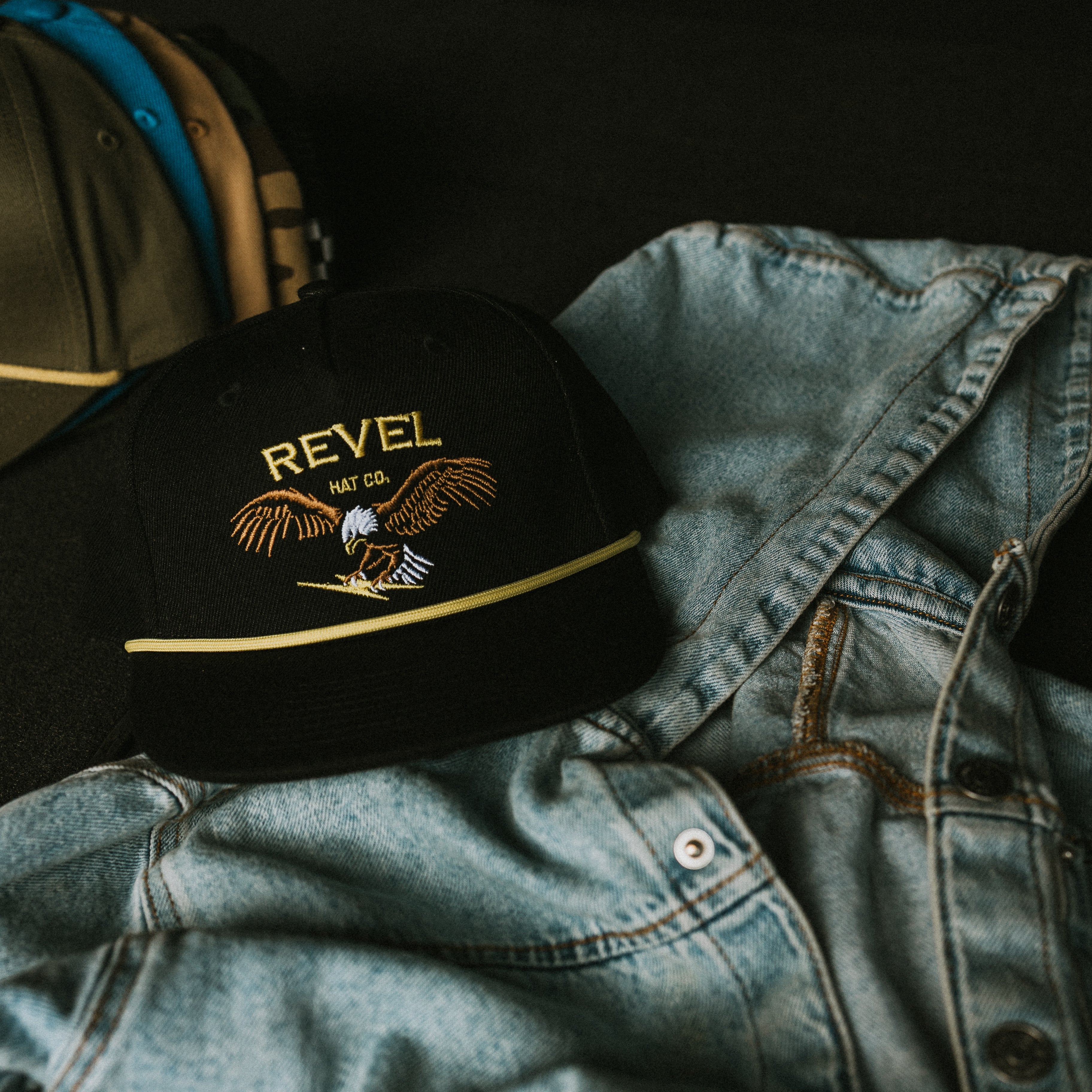 Black cap with eagle snapback for kids on a denim jacket against a dark background