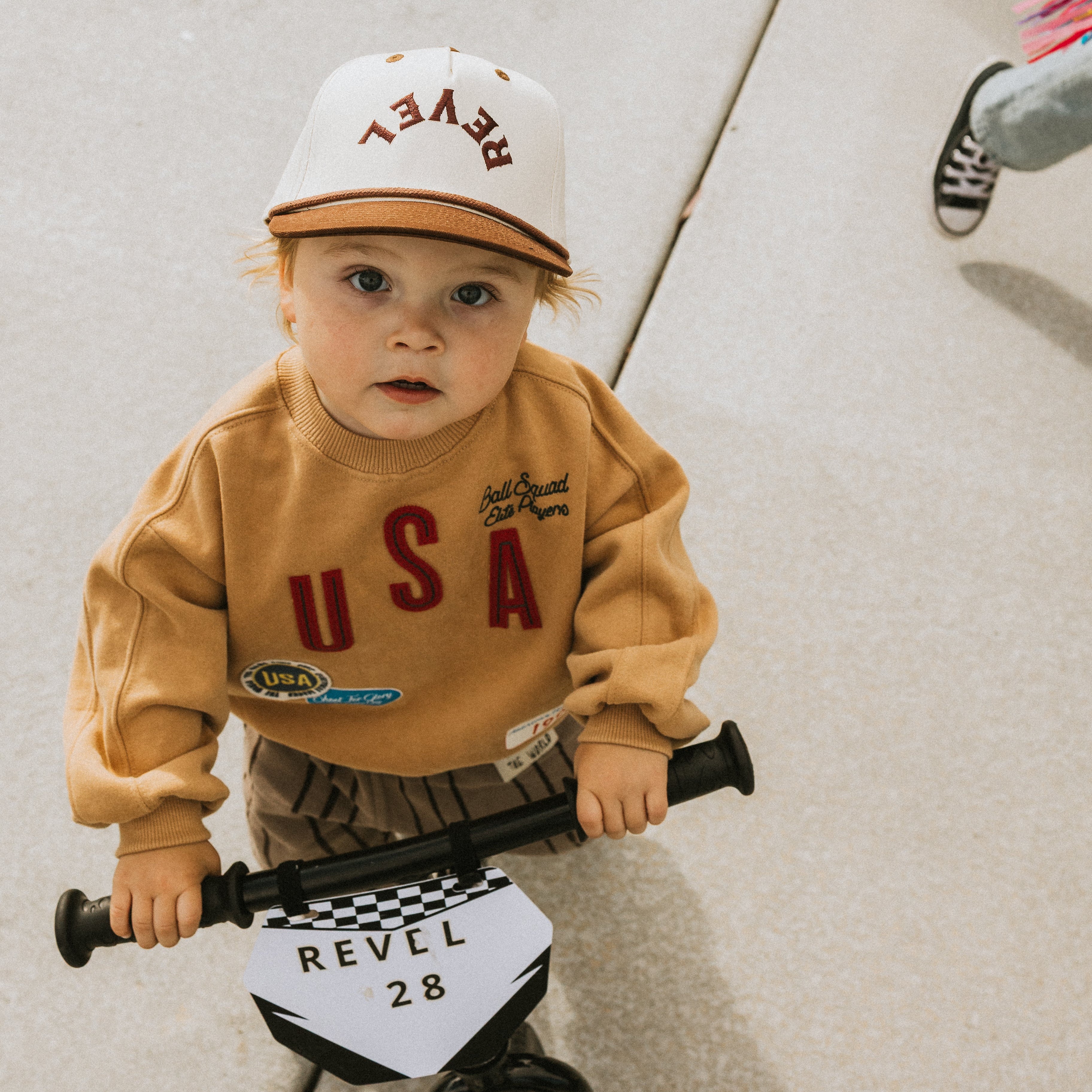 Child wearing a snapback cap and sweatshirt, holding a bike with a checkered flag design.