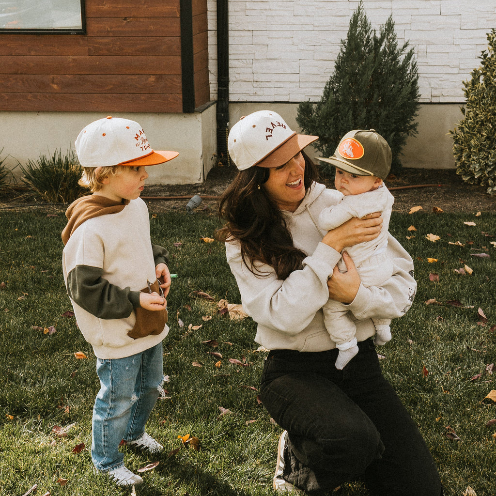 Woman and two children wearing matching snapback hats in a grassy area.