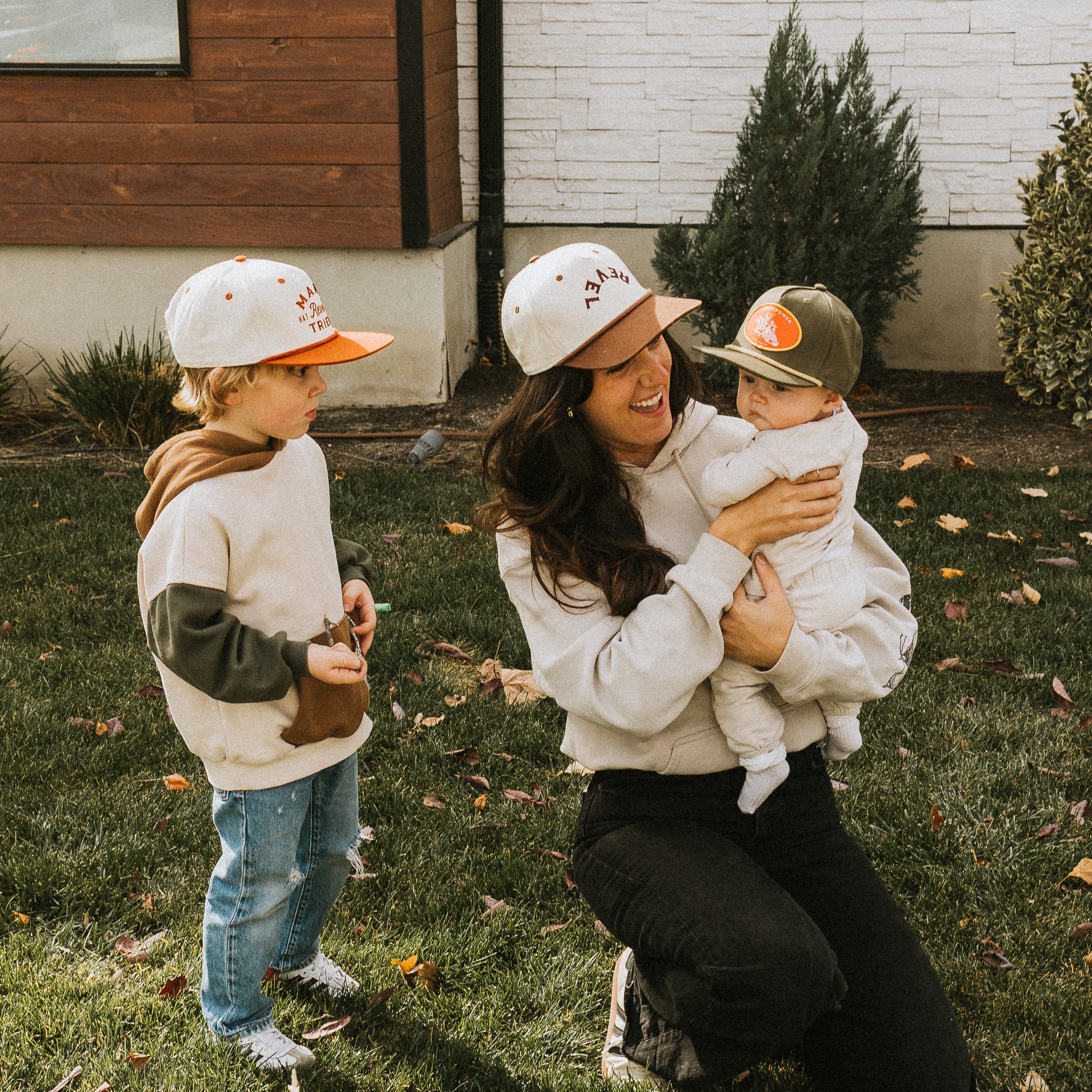 Woman and two children wearing matching snapback hats in a grassy area.