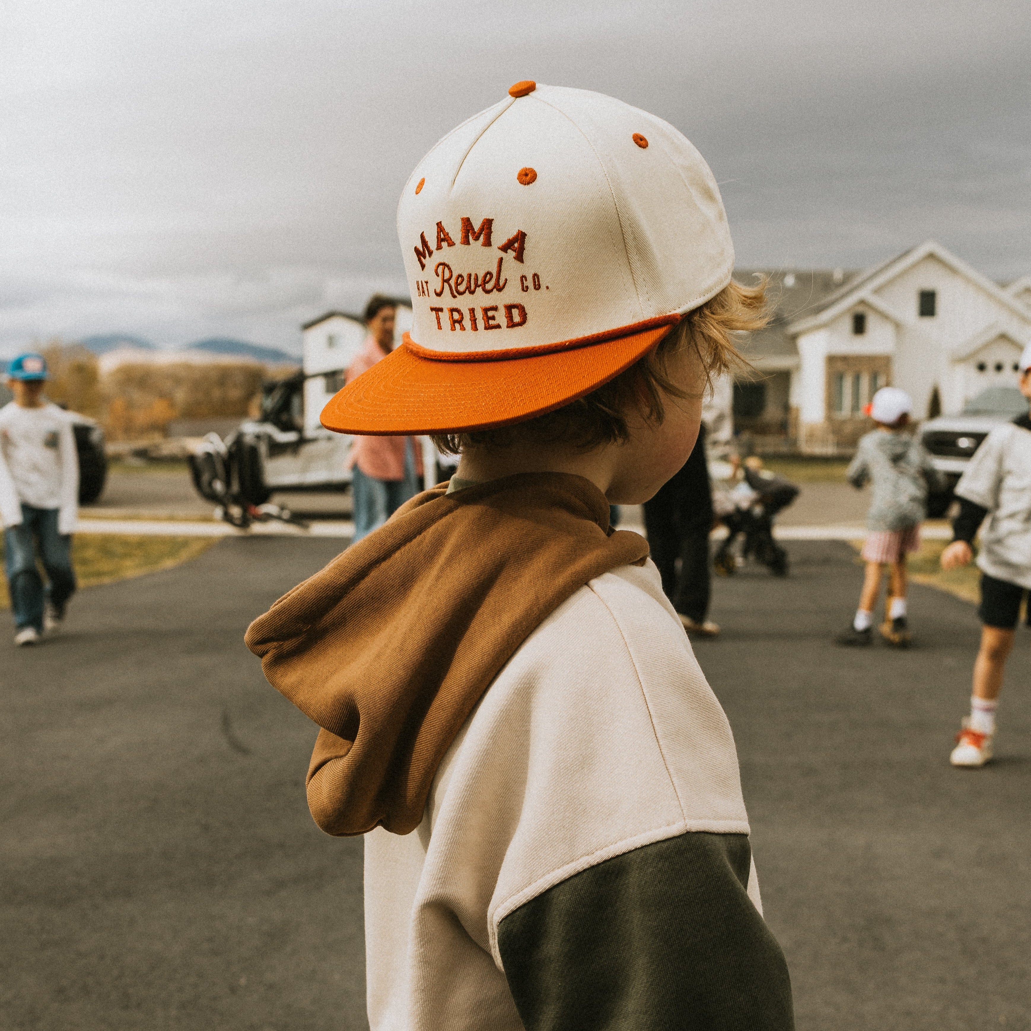 Child wearing a snapback cap with text saying "mama tried", with kids playing in the background