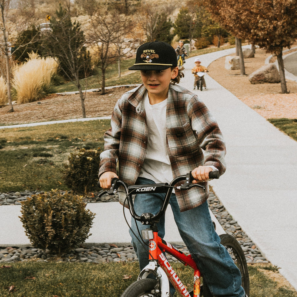 Boy riding bike wearing a black vintage inspired snapback with an embroidered eagle. 