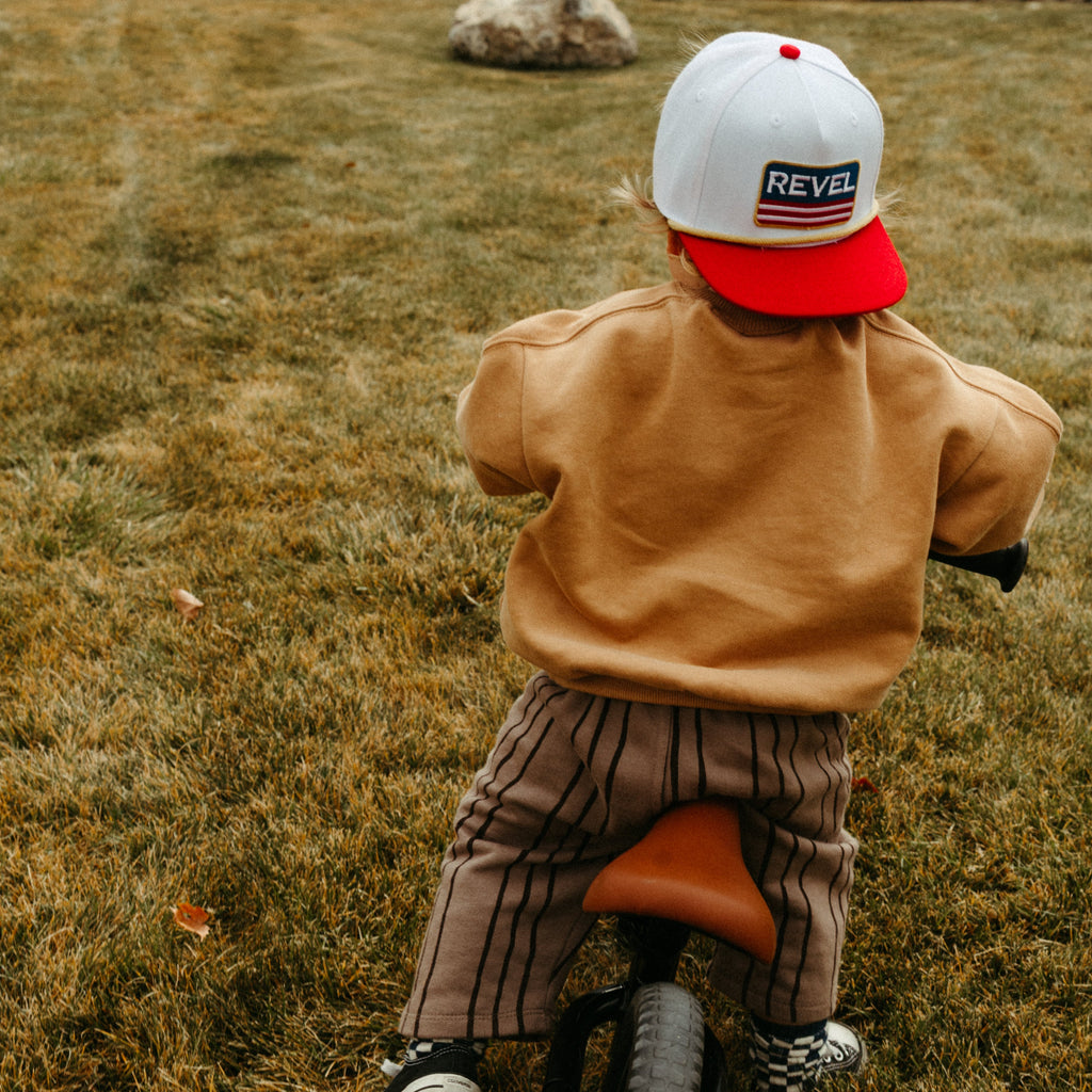 Child wearing a red and white snapback hat riding a bike in a grassy field.